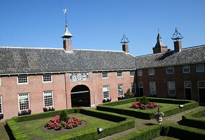 a red brick building with black roof and formal garden